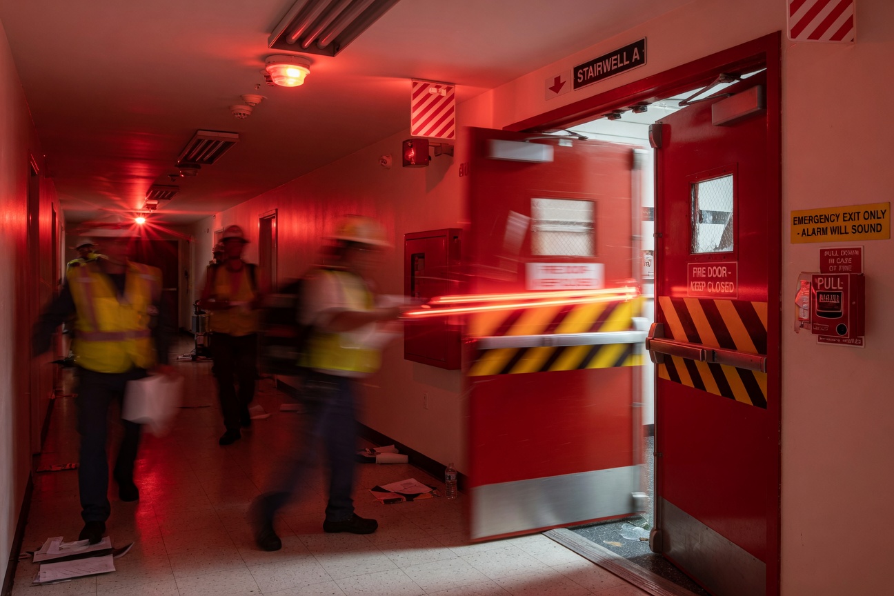 Dramatic 8K image showing fire door closing sequence in slow motion during fire drill, motion blur on door, red emergency lighting in commercial hallway